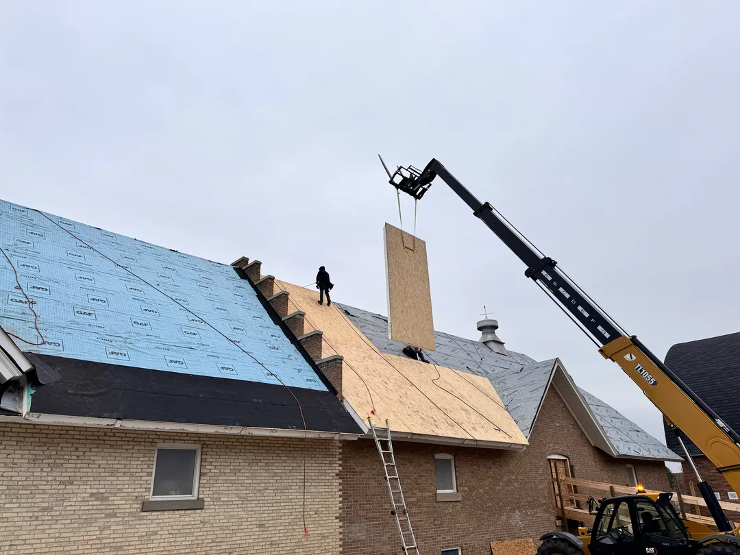 A Falcon Roofing crew re-roofing a large building with GAF underlayment and a telehandler on site.