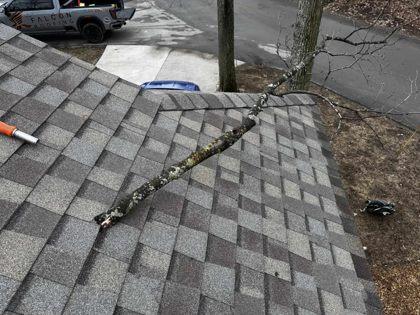A fallen tree branch on a storm-damaged roof, with a Falcon Roofing truck on site in Traverse City.